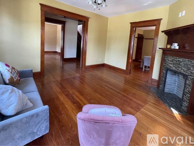A living room with a grey couch, a pink chair, and a fireplace.
