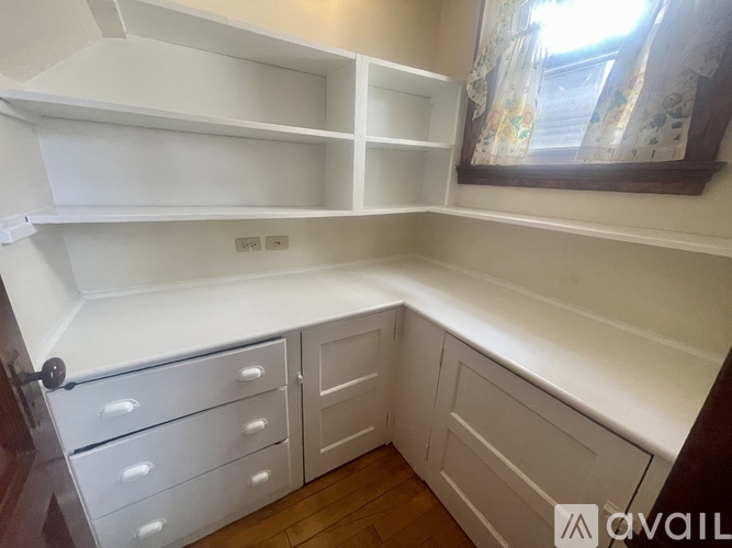 A white pantry with a window and a wooden floor.