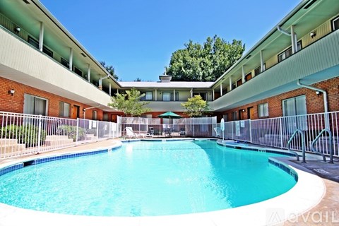 A large swimming pool is surrounded by a metal fence and a building with red brick walls.