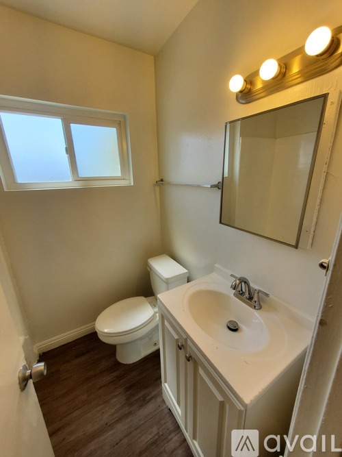 A bathroom with a toilet, sink, mirror, and window.