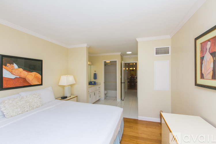 A bedroom with a bed, a nightstand with a lamp, and a painting on the wall.