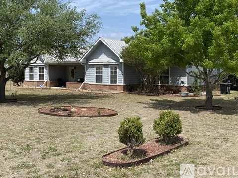 A house with a grey roof and a white fence is surrounded by a grassy area with trees and bushes.
