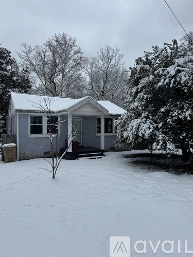 A small house with a snow-covered roof and a bare tree in front.