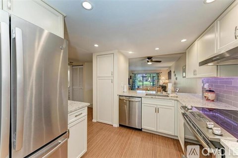 A modern kitchen with a stainless steel refrigerator and wooden flooring.