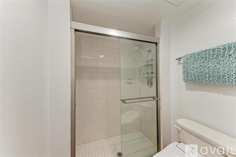 A white bathroom with a glass shower door and a white towel hanging on the wall.