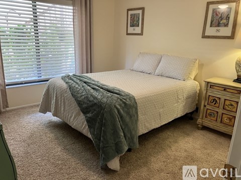 A bedroom with a bed, nightstand, and window with blinds.