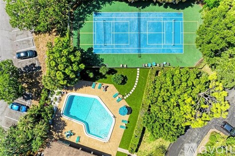 An aerial view of a tennis court and a swimming pool surrounded by trees.