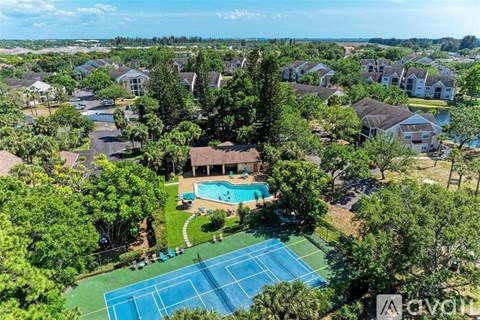 A tennis court is surrounded by trees and houses.