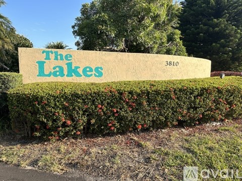 A sign that says "The Lakes" is in front of a hedge.