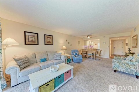 A living room with a grey couch, a white coffee table, and a dining area in the background.