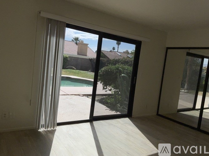 A room with a view of a pool and a house through the sliding glass doors.