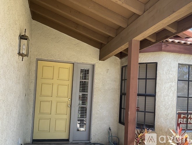 A yellow door is on the left side of a house with a sign that says "For Rent" on the right.