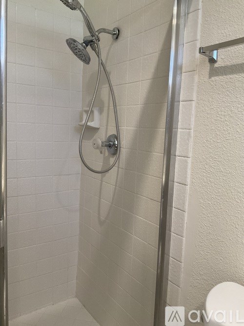 A white tiled shower with a silver shower head and hand held shower.