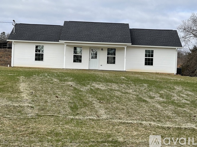 A white house with a black roof is situated in a grassy field.
