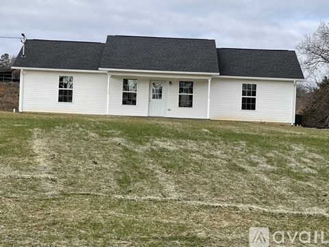 A white house with a black roof is situated in a grassy field.