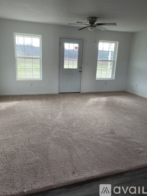 A room with a carpeted floor, a ceiling fan, and a door leading to a balcony.