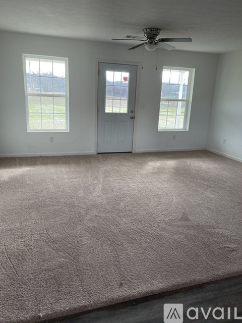 A room with a carpeted floor, a ceiling fan, and a door leading to a balcony.