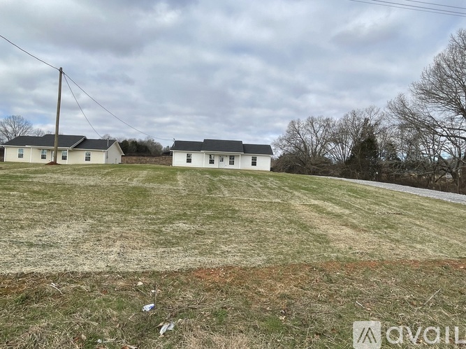 A grassy field with a white house and a telephone pole in the background.