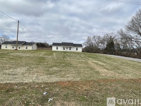 A grassy field with a white house and a telephone pole in the background.