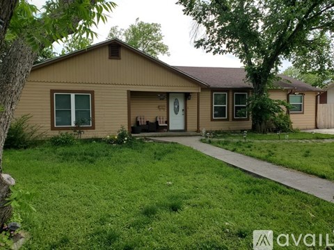 A house with a brown siding and a white door is surrounded by a green lawn.
