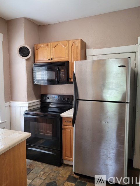 A kitchen with a black oven and microwave, wooden cabinets, and a silver refrigerator.