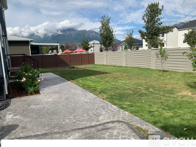 A backyard with a paved walkway leading to a fence and houses in the background.