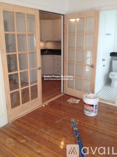 A room with wooden floors and a doorway leading to a kitchen.