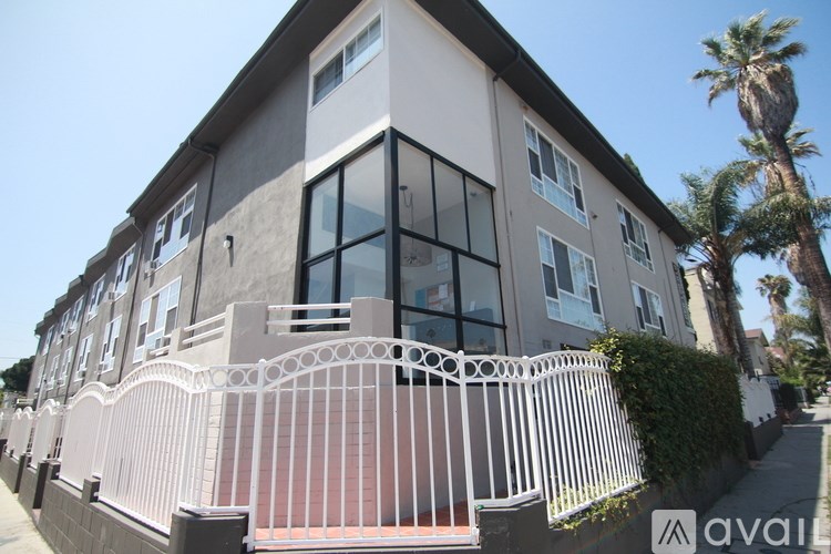 A modern two-story house with a white fence and a palm tree in front.