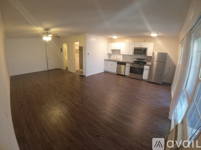 A spacious room with wooden floors and a kitchen area with stainless steel appliances.