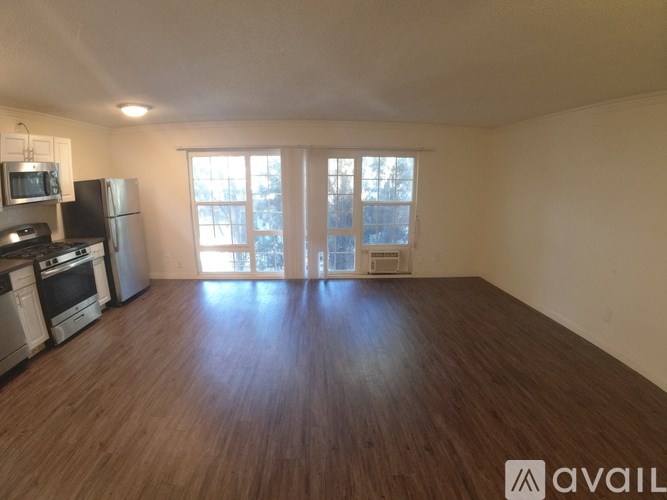 A spacious living room with hardwood floors and a kitchen area with appliances.