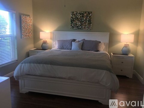 A bedroom with a large bed, two nightstands with lamps, and a floral picture on the wall.