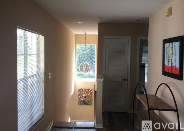 A room with a window, a door, a bench, and a painting on the wall.