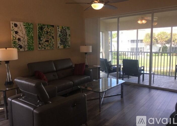A living room with a grey leather couch, a glass table, and a ceiling fan.