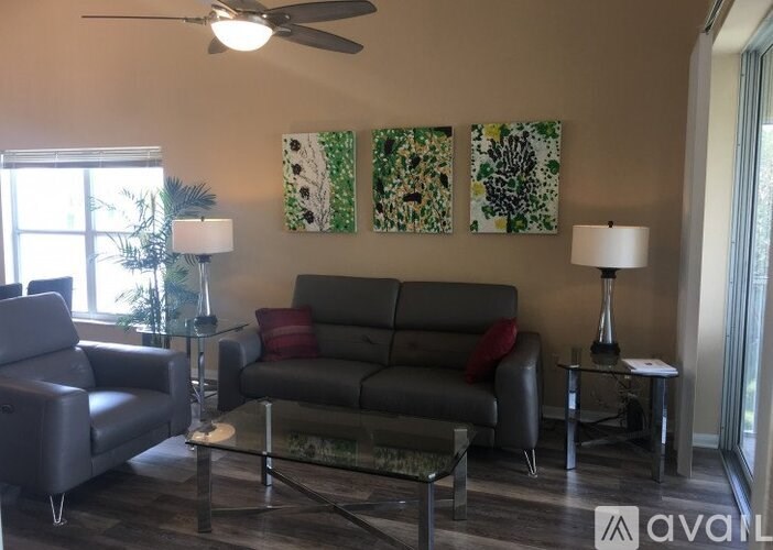 A living room with a grey couch, a black chair, a glass table, and two lamps.