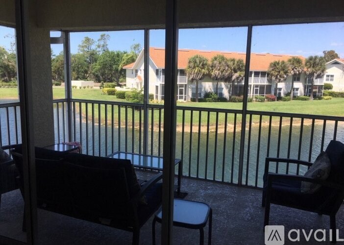 A balcony with two chairs and a table overlooking a green field and buildings.