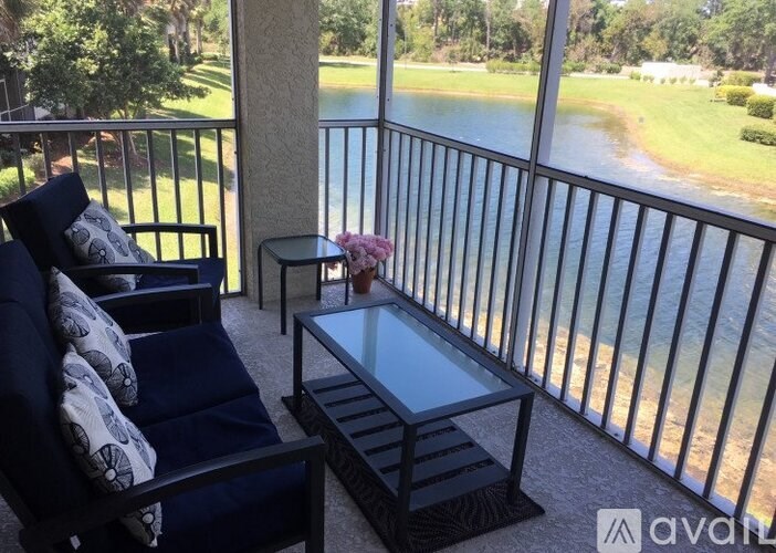 A balcony with a black sofa and a glass table with a vase of flowers on it.