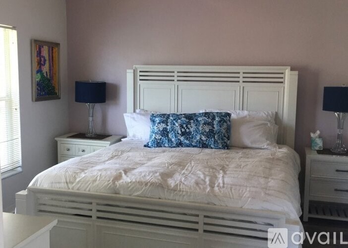 A white bed with a blue pillow and two lamps on either side.