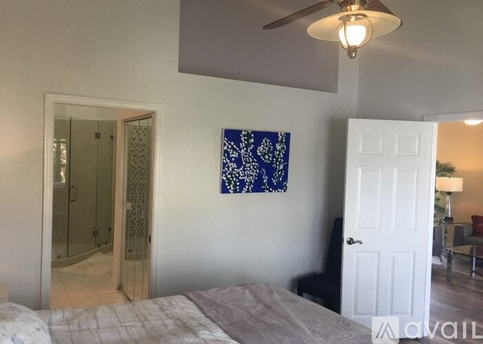 A bedroom with a bed, a ceiling fan, and a painting on the wall.
