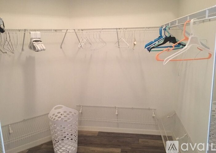 A white closet with clothes hanging and a white laundry basket on the floor.