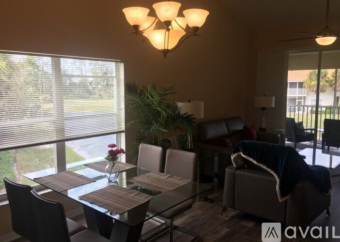 A living room with a glass table and chairs, a ceiling fan, and a large window with blinds.