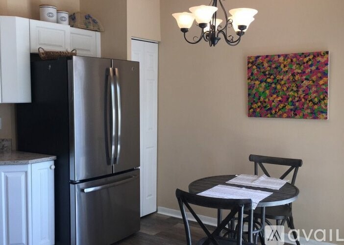 A kitchen with a refrigerator, a table with chairs and a painting on the wall.