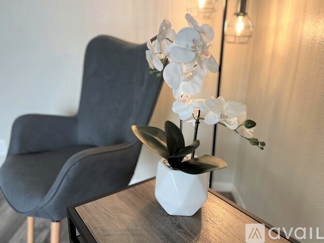 A black chair sits next to a table with a vase of white flowers on it.