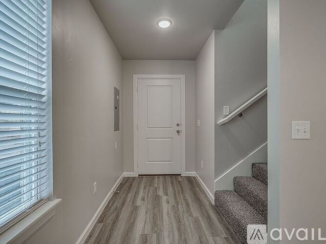A hallway with a wooden floor, a white door, and a staircase with a grey carpet.