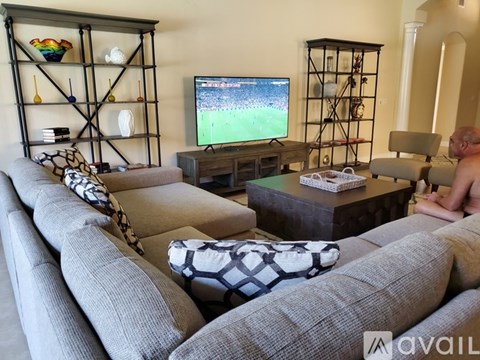 A man is sitting on a couch in a living room with a television playing a soccer game.