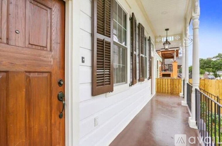 A wooden door is on the left of a porch with a white wall and brown shutters.