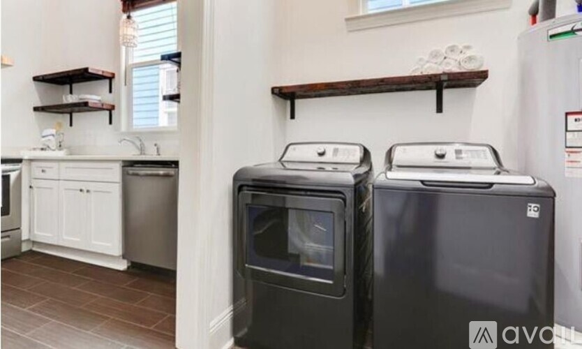 Two black ovens in a kitchen with white cabinets and a wooden shelf.