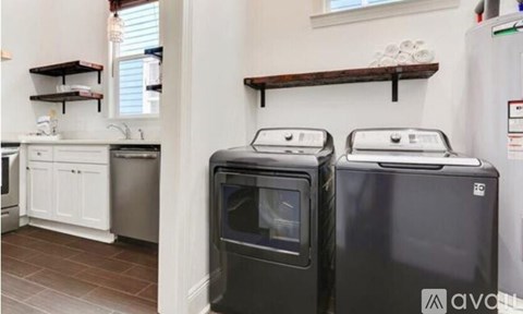 Two black ovens in a kitchen with white cabinets and a wooden shelf.
