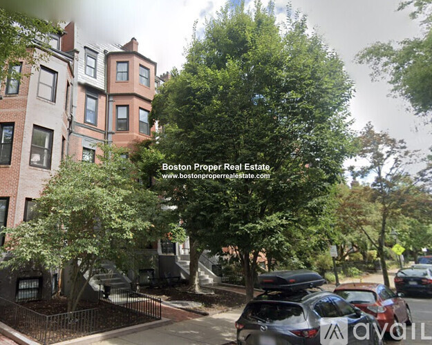 A street view with parked cars and a building with the text "Boston Proper Real Estate" on it.