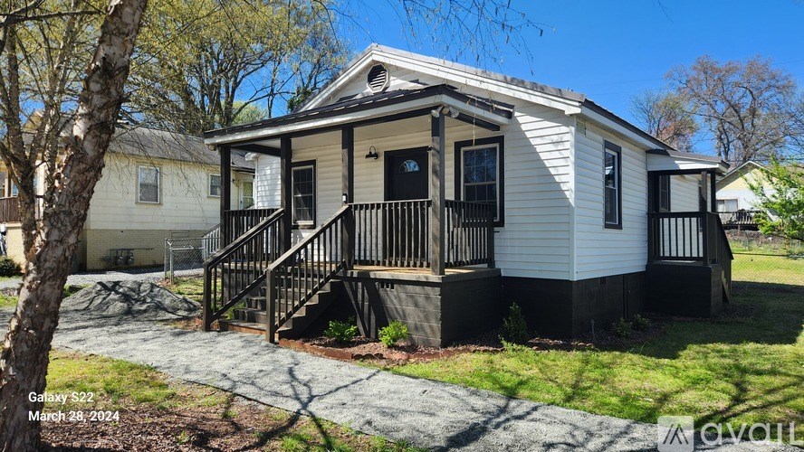 A small white house with a black front porch and a tree in front.