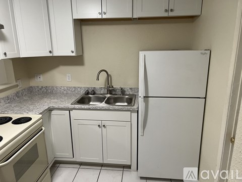 A kitchen with a white refrigerator, sink, and cabinets.